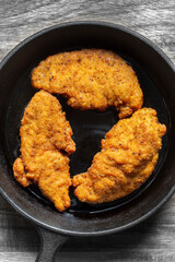 Southern fried chicken cooked in a cast iron frying pan with cooking oil. On a wooden board background..