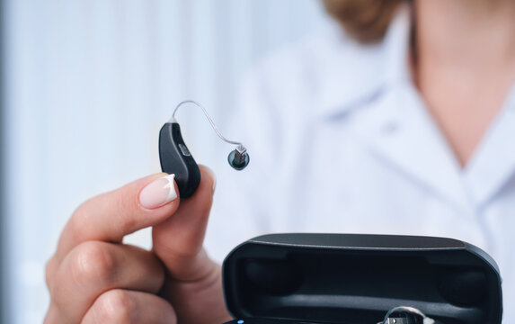 Patient charging hearing aid in special portable Smart Charger with built-in power bank. Case in man hands keeps hearing aids dry and safe
