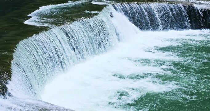 Powerful waterfall cascading over a ledge into a churning river, showing the force of nature.
