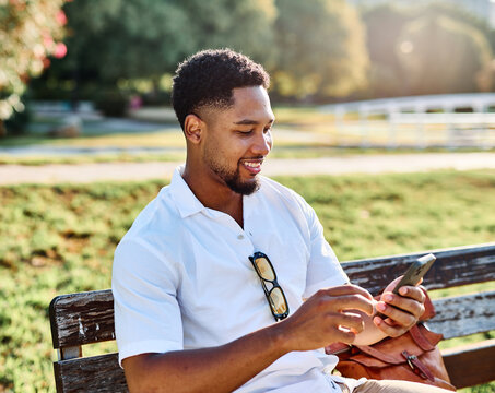 Young man enjoys sunny day while using smartphone in urban setting, highlighting his joy and connection to the world around him
