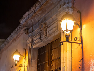 The two street lamps are glowing brightly, illuminating the building and the area around it. Historic center of Queretaro, colonial architecture, decorations for the celebration of Mexico's Independen