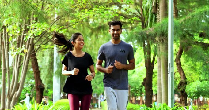 Indian young couple jogging in park together enjoying healthy morning routine and fitness oriented start of the day, spending quality time outdoors breathing fresh air surrounded in sunshine