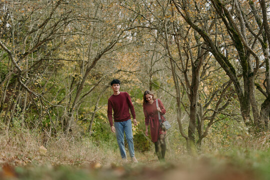A candid outdoor portrait of a young couple walking through an autumn woodland path, natural expressions and relaxed posture conveying authentic connection and credible everyday intimacy.