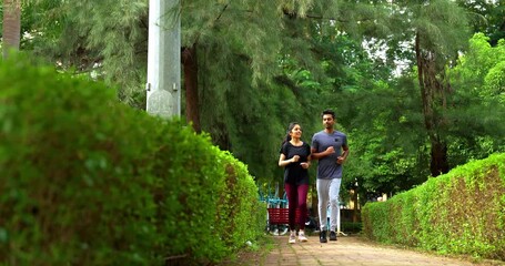 Indian young couple jogging in park together enjoying healthy morning routine and fitness oriented start of the day, spending quality time outdoors breathing fresh air surrounded in sunshine