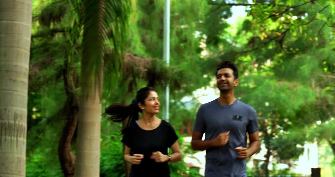 Indian young couple jogging in park together enjoying healthy morning routine and fitness oriented start of the day, spending quality time outdoors breathing fresh air surrounded in sunshine