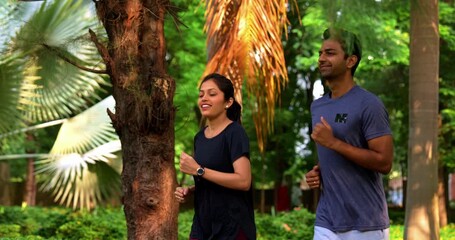 Indian young couple jogging in park together enjoying healthy morning routine and fitness oriented start of the day, spending quality time outdoors breathing fresh air surrounded in sunshine