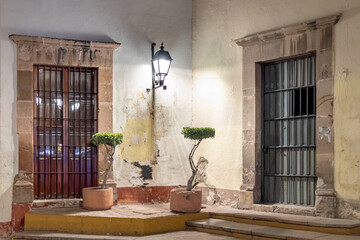 A building with two doors and a lamp post in front of it. The lamp post is lit up at night. Historic center of Queretaro, colonial architecture, decorations for the celebration of Mexico's Independenc