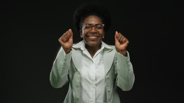 Woman smiling confidently over isolated black background wearing glasses and green suit representing positivity and joy.