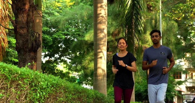 Indian young couple jogging in park together enjoying healthy morning routine and fitness oriented start of the day, spending quality time outdoors breathing fresh air surrounded in sunshine