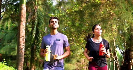 Indian young couple jogging in park together enjoying healthy morning routine and fitness oriented start of the day, spending quality time outdoors breathing fresh air surrounded by trees