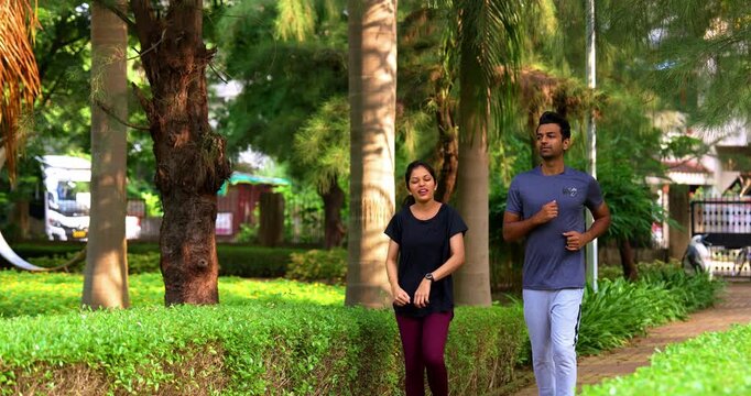 Indian young couple jogging in park together enjoying healthy morning routine and fitness oriented start of the day, spending quality time outdoors breathing fresh air surrounded by trees