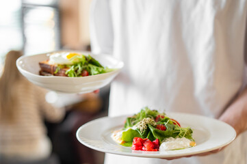 Waiter holding two plates with gourmet egg salad and toast in a busy restaurant. Fresh ingredients, professional service, and vibrant dining atmosphere.