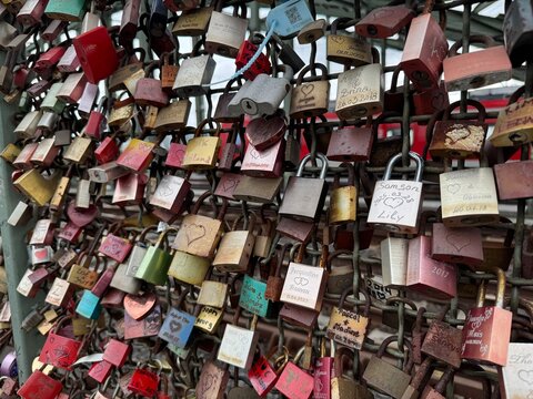 Close-up view of hundreds of colorful love locks attached to a bridge fence, each engraved with names and dates symbolizing love, unity, and everlasting commitment.