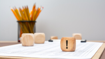 Wooden cube with exclamation mark on financial document and plain background