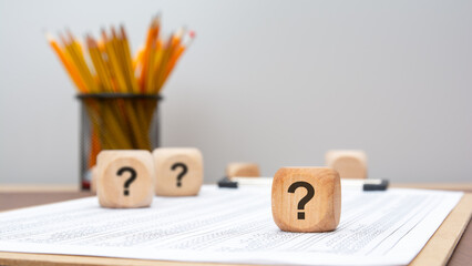 wooden cubes with question marks on financial report, symbol of doubt or uncertainty