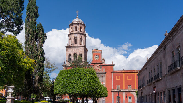 A large red building with a clock tower and a green tree in front of it. The sky is blue. Historic center of Queretaro, colonial architecture, decorations for the celebration of Mexico's Independence  - Powered by Adobe