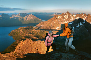 Obraz premium Couple hiking in Norway man helps woman climbing mountains healthy lifestyle outdoor active family vacations adventure tour, friends mountaineering together boyfriend and girlfriend relationship