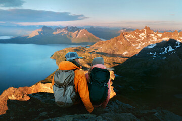 Couple hiking in Norway friends man and woman travel outdoor active vacations lifestyle romantic trip, family adventurers boyfriend and girlfriend tourists enjoying sunset fjord view from mountain top