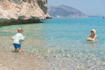 Sunny Mediterranean beach with family enjoying crystal-clear water and natural cliffs, Cala Luna,...