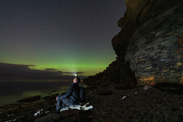 Hiker with a headlamp watches the amazing Aurora Borealis on a rocky beach at the Paldiski...
