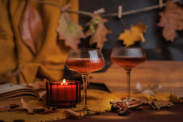 Two coupe glasses with rose champagne and candle on autumn table with leaves and spices