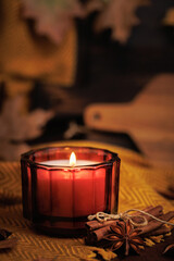 Candle flame in red glass surrounded by yellow fabric cinnamon star anise and autumn leaves