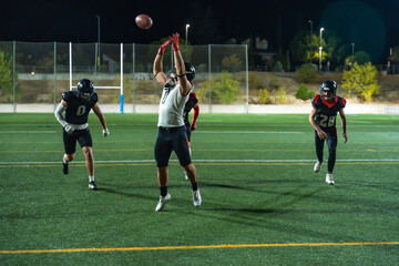 American football receiver jumping to catch pass at night