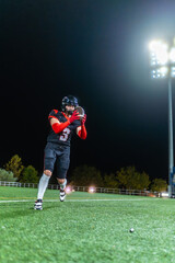 Naklejka premium American football player catching ball on field at night