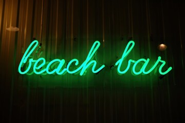 Neon beach bar sign glows green at night against dark facade