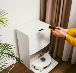 Control of robot vacuum cleaner with smartphone in female hands before cleaning in beautiful modern apartment
