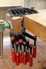 Mehrere Schraubzwingen mit roten Griffen sind ordentlich an einer Werkbank befestigt. Das Motiv steht f&uuml;r Handwerk, Ordnung in der Werkstatt und professionelle Arbeitsmittel.