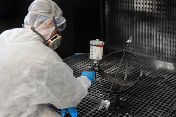 Person in Schutzkleidung arbeitet in einer technischen Kabine und reinigt bzw. beschichtet ein Bauteil mit professioneller Ausr&uuml;stung. Das Motiv steht f&uuml;r Arbeitssicherheit, Industrieprozesse und pr&auml;z