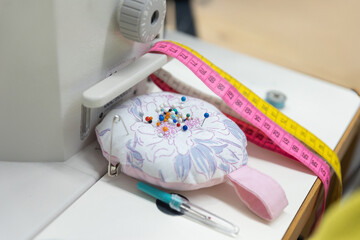 N&auml;hutensilien wie Nadelkissen, Ma&szlig;band, Schere und N&auml;hmaschine liegen bereit auf einem Arbeitstisch. Das Motiv steht f&uuml;r Handarbeit, Kreativit&auml;t und textile Gestaltung.