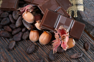 Broken dark chocolate with cocoa beans and hazelnuts on a wooden table