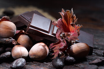 Broken dark chocolate with cocoa beans and hazelnuts on a wooden table