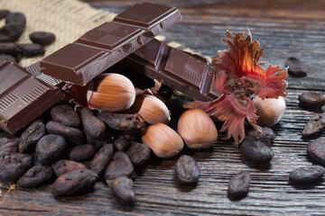 Broken dark chocolate with cocoa beans and hazelnuts on a wooden table