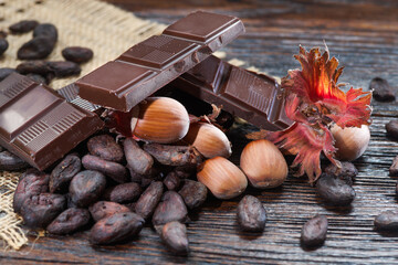 Broken dark chocolate with cocoa beans and hazelnuts on a wooden table