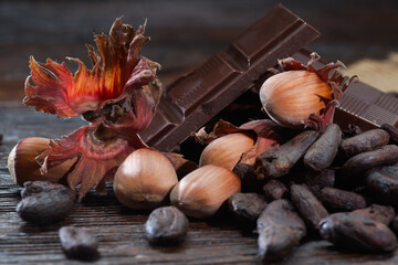 Broken dark chocolate with cocoa beans and hazelnuts on a wooden table