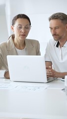 Businessman and adult businesswoman reviewing marketing analytics on laptops, working together strategically in contemporary office workplace. Business people concept