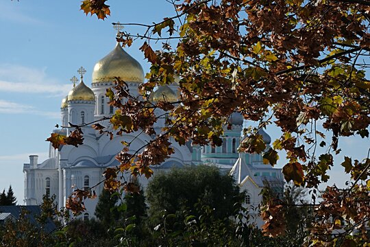 Spiritual atmosphere of the Diveyevo Monastery, Russia: a view of the golden dome of an Orthodox church peeking through picturesque autumn leaves. 