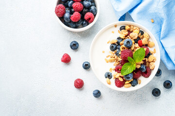 Yogurt with fresh berries and granola on white table.