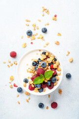 Yogurt with fresh berries and granola on white table.