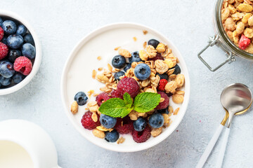 Yogurt with fresh berries and granola on white table.