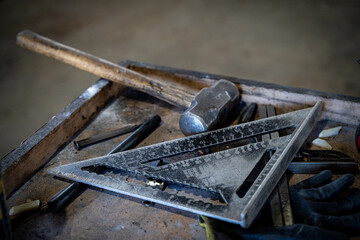 Close up of metal square ruler and hammer on workshop table.