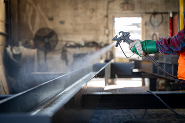 Worker spray painting metal beam in industrial workshop.