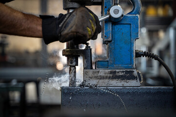 Worker using a magnetic drill press on a steel beam in a workshop.