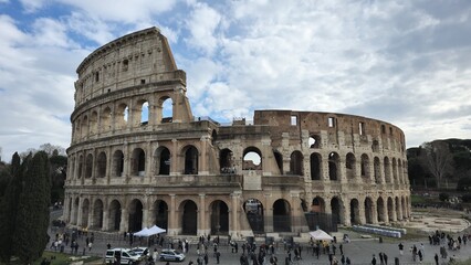 Obraz premium Rome, Italy - 13 January 2025. The Colosseum’s facade shows layered arcades and partial ruins as tourists gather around its grand, elliptical structure.