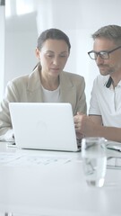 Obraz premium Businessman and adult businesswoman reviewing marketing analytics on laptops, working together strategically in contemporary workplace with minimalist interior design and collaborative atmosphere
