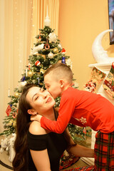 A woman and a boy sitting on the floor in front of a decorated Christmas tree. Garlands, ornaments, and baubles glitter on the tree. The comfort and joy of a family holiday