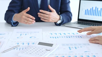 Business professionals collaborating at a conference table, reviewing financial charts and reports, using a laptop and calculator while engaging in discussions about strategy and performance